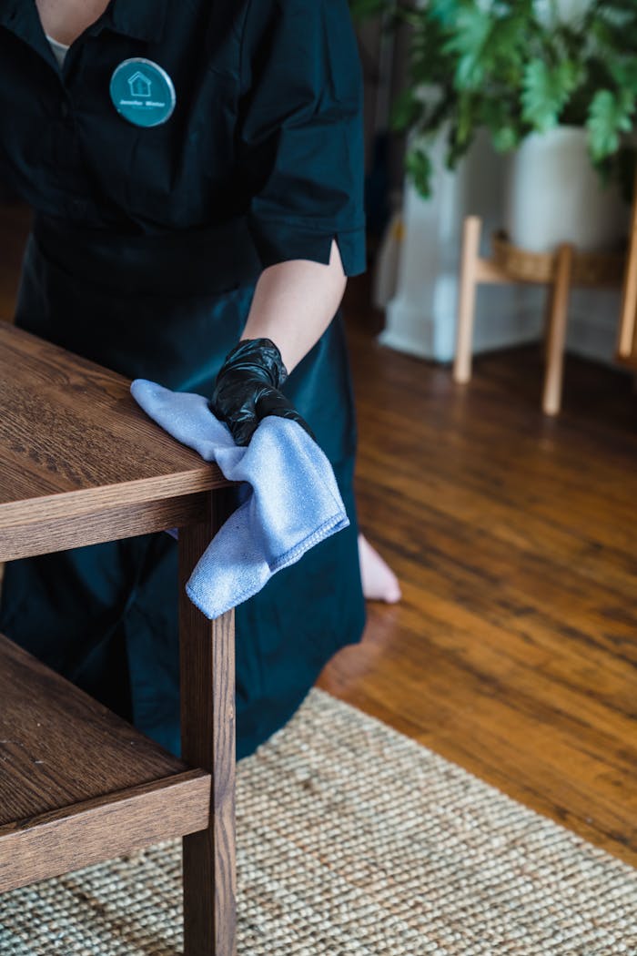 Person in uniform cleaning a wooden table indoors with a cloth.