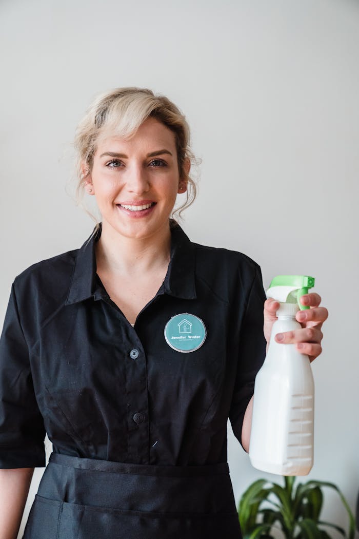 Smiling woman in uniform holding a spray bottle, symbolizing professional cleaning services indoors.